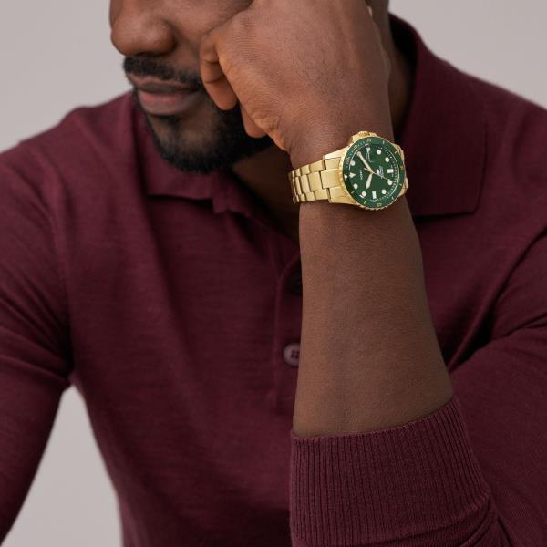 Men's gold steel dive watch with green dial on wrist, date window visible