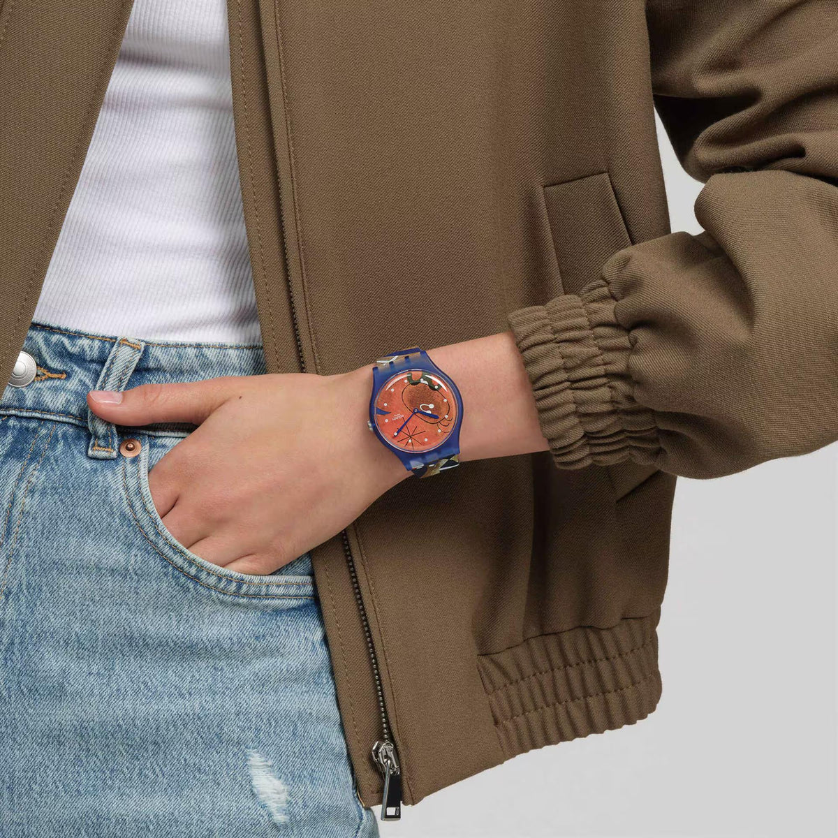 Blue silicone strap watch on wrist over denim with orange bird dial