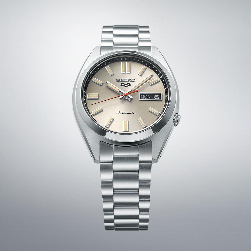 Seiko 5 Sports SNXS Classic watch showing a cream dial and stainless steel bracelet on a gray background