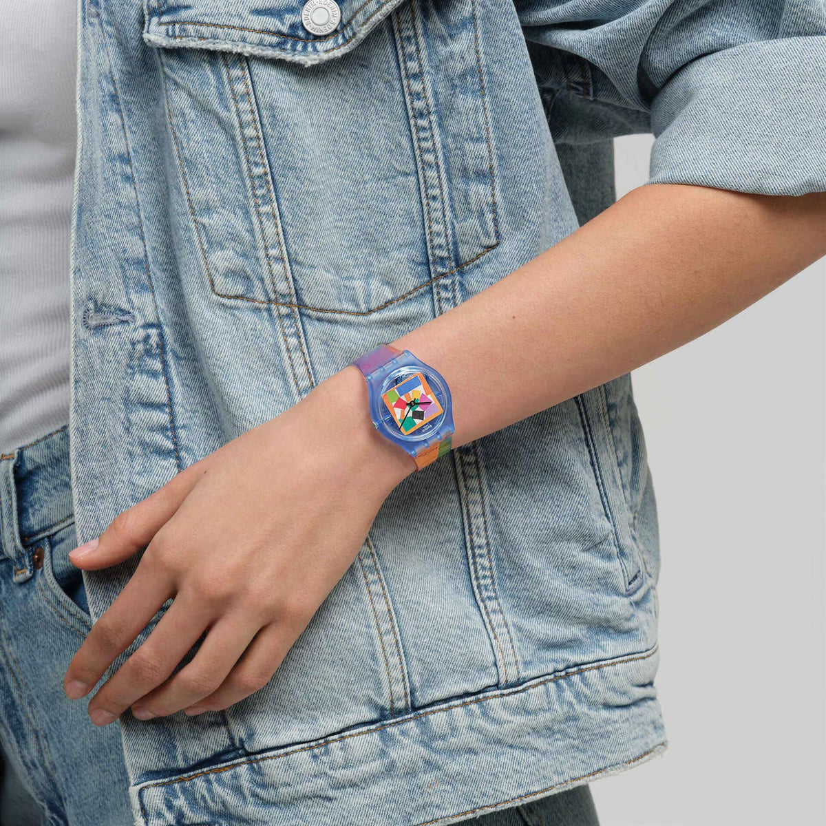 Swatch wristwatch on wrist with colorful geometric dial, clear strap with graphic band