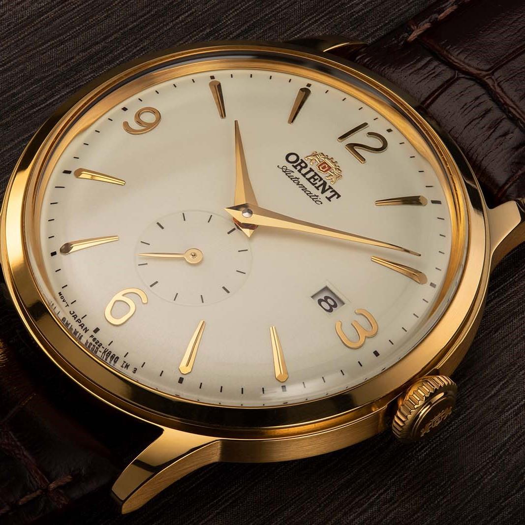 Gold-tone automatic wristwatch with white dial, gold markers, and brown leather strap