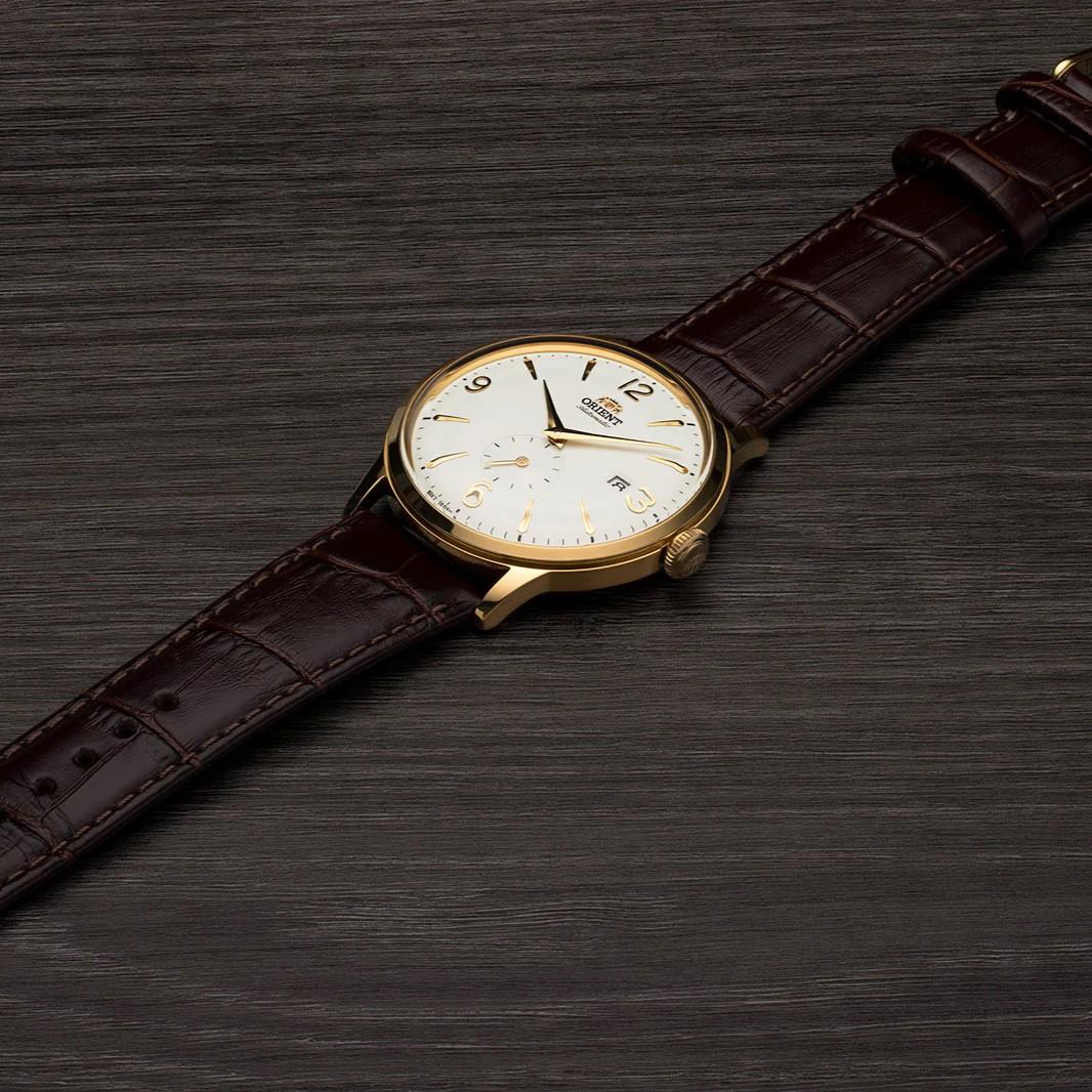 Gold-tone automatic wristwatch with white dial and brown leather strap, side profile