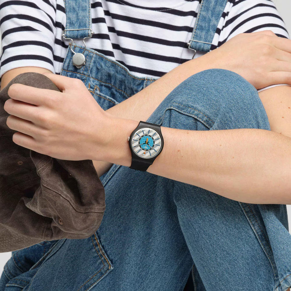 Swatch bioceramic wristwatch on denim outfit; black silicone strap, blue center dial.
