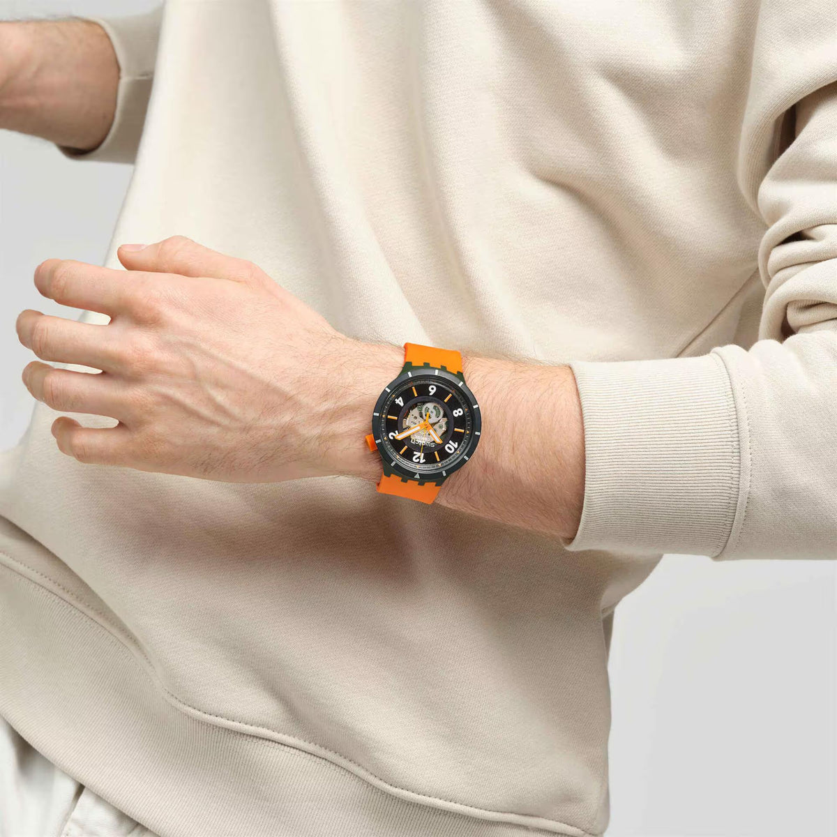 Swatch watch on wrist with black skeleton dial and orange-and-green silicone strap