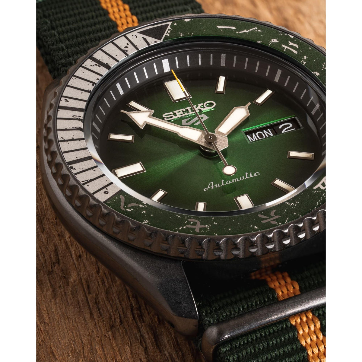 Men's automatic wristwatch with green dial, raised bezel, and orange fabric strap.