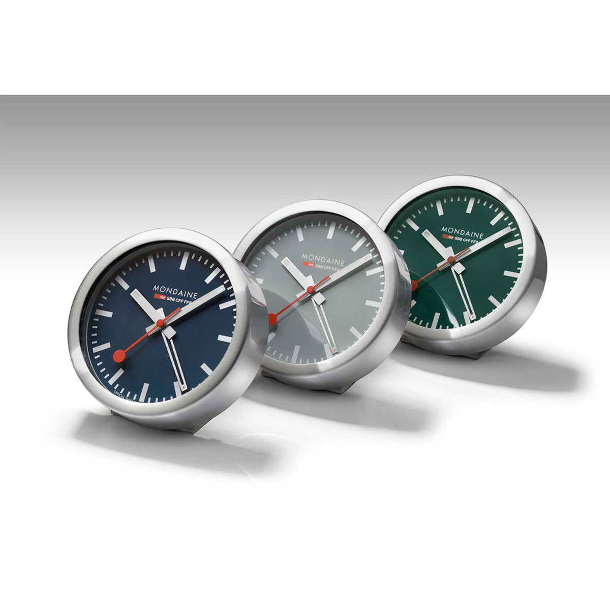 Three round table alarm clocks with brushed metal bodies and blue, grey, green dials.