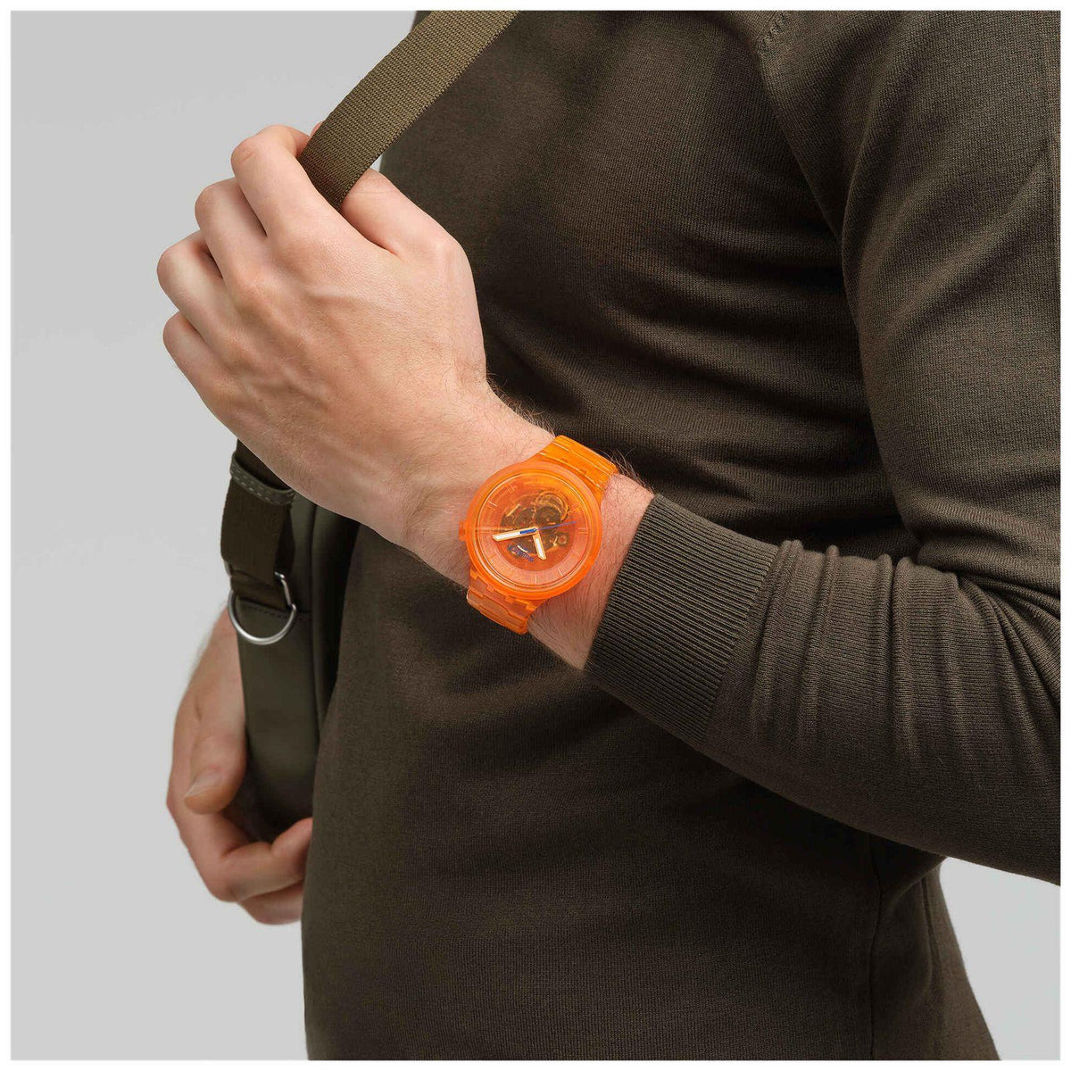 Orange Swatch bio-sourced watch on wrist with orange dial, worn with dark long-sleeve.