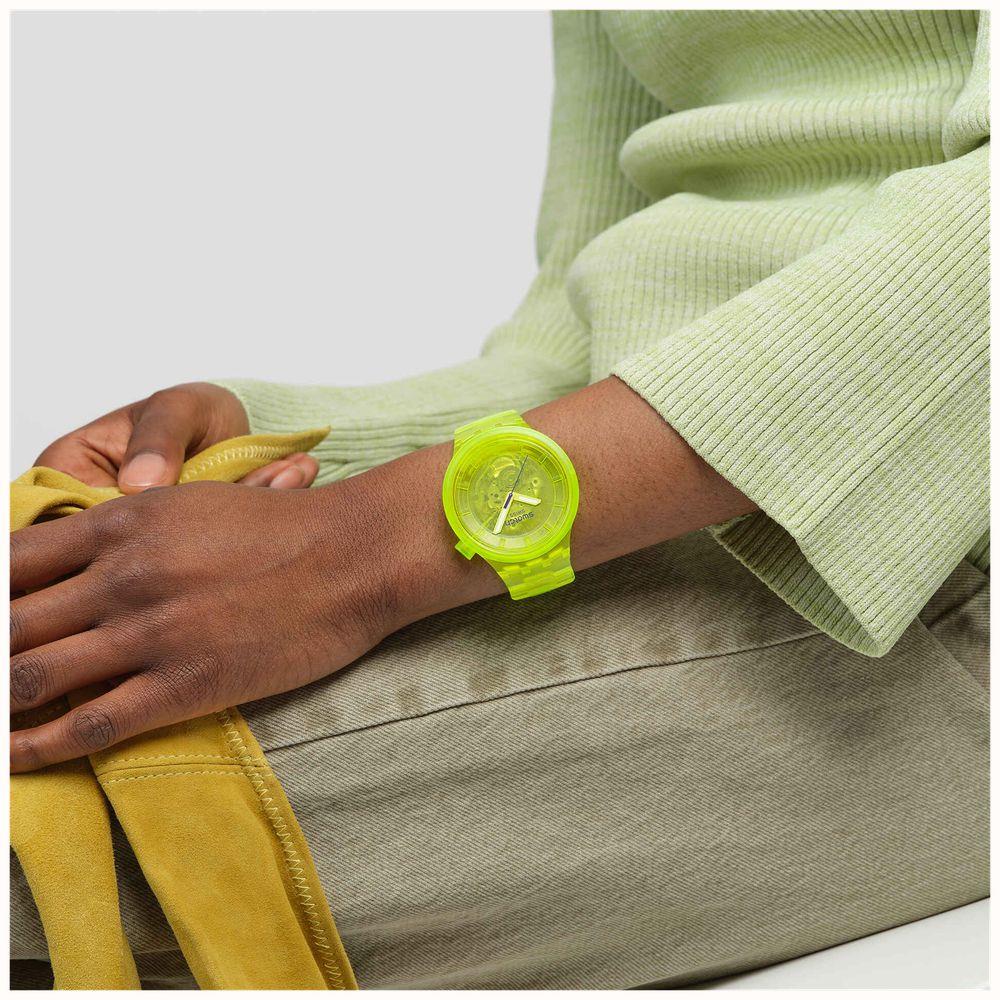 Neon yellow Swatch Joy wristwatch on forearm, round yellow dial and clear strap