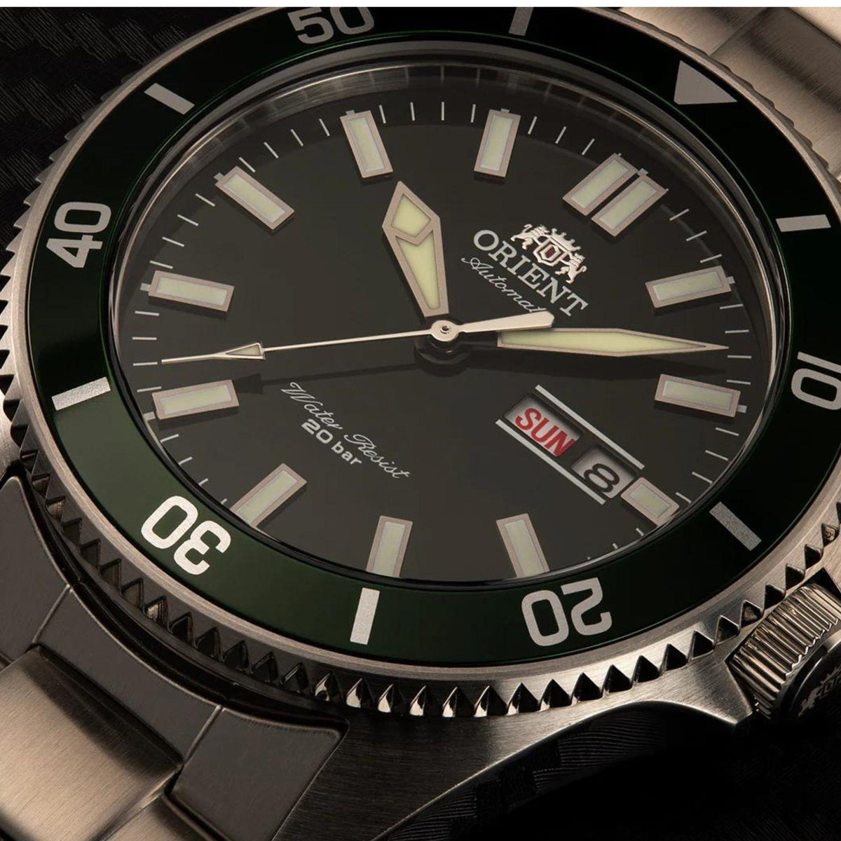 Green dial automatic watch close-up with baton markers, hands, and day-date window.