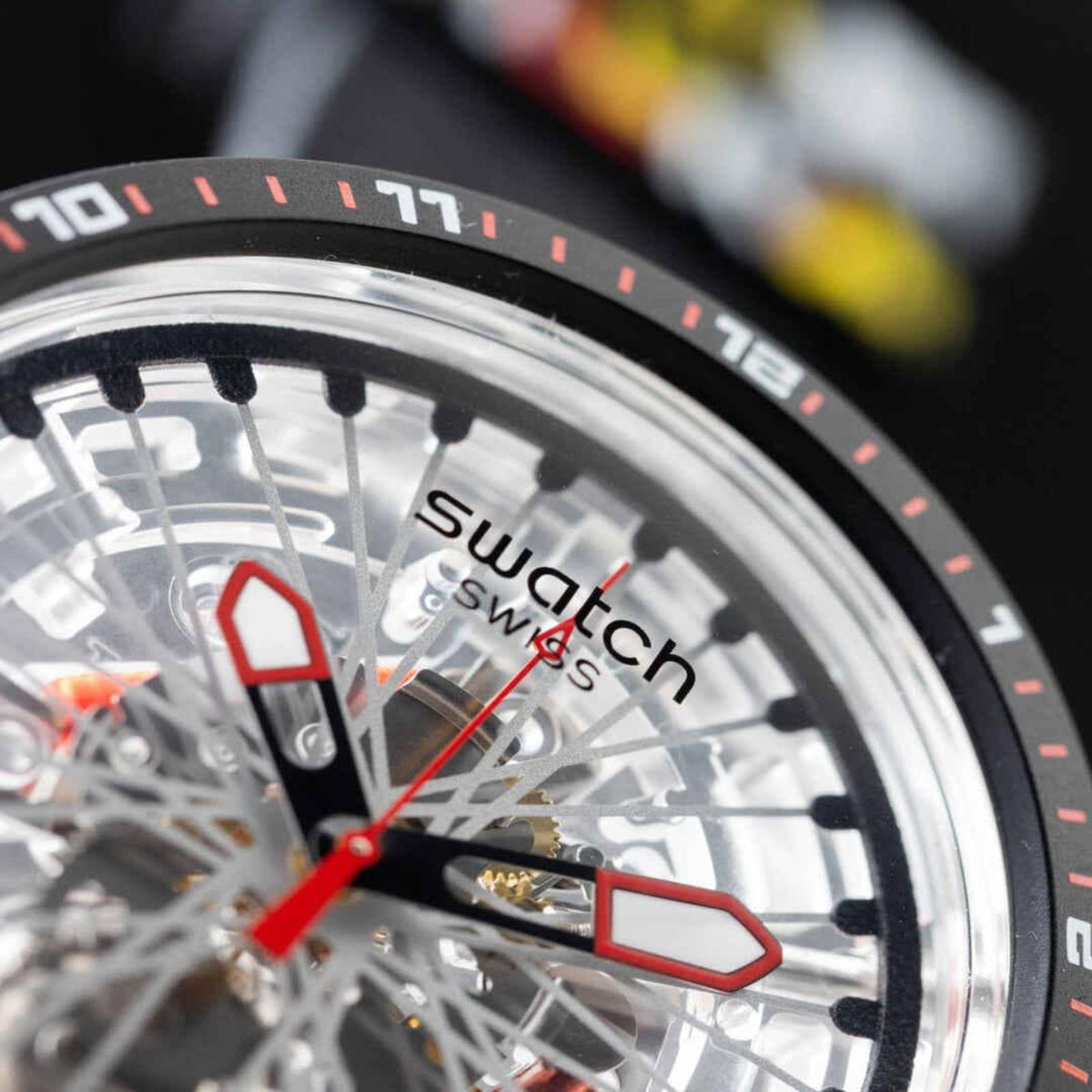 Swatch transparent dial wristwatch close-up with red indices and hands, black bezel