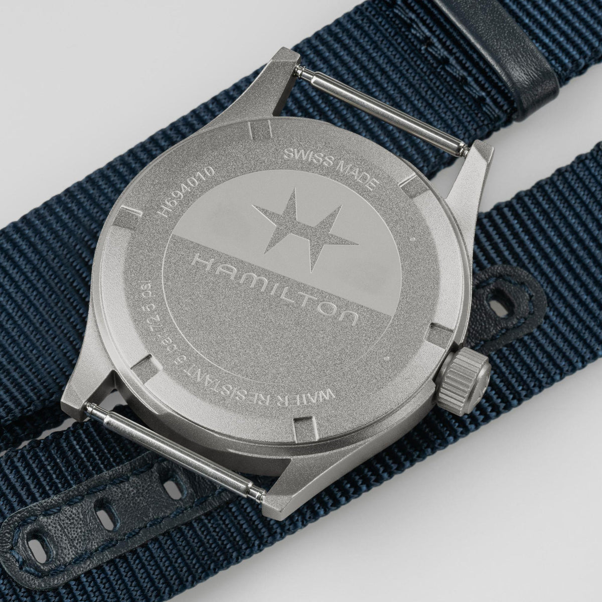 Watch case back with star emblem and crown, mounted on dark blue NATO strap