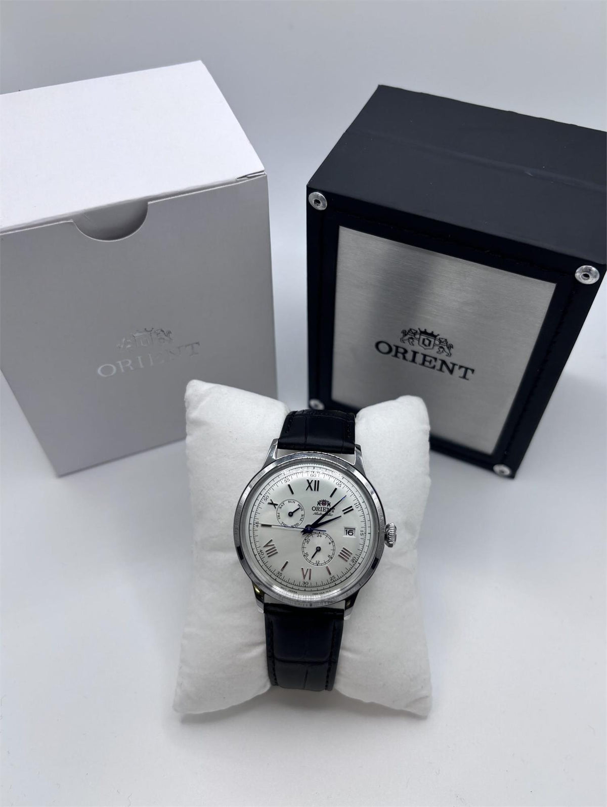 Men's automatic wristwatch with black leather strap, white dial, and blue hands on display.