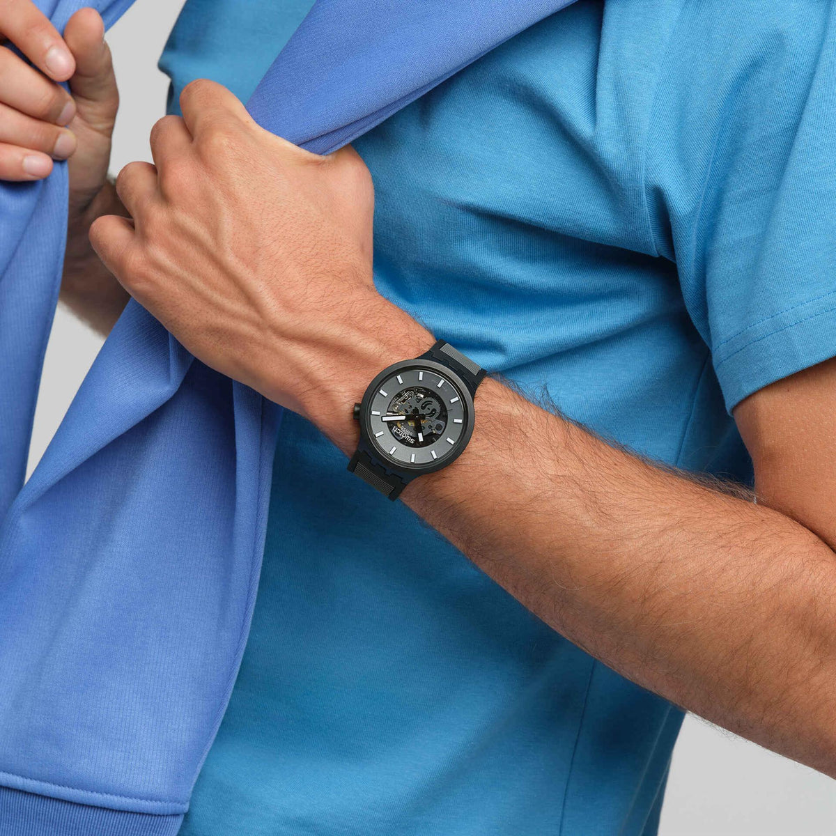 Men's quartz watch on wrist with black rubber strap, dark skeleton dial, baton markers.