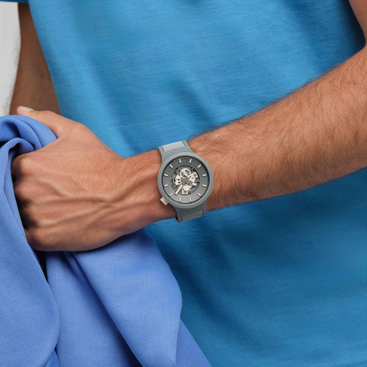 Swatch quartz watch on wrist with gray silicone strap and blue-gray dial, analog hands