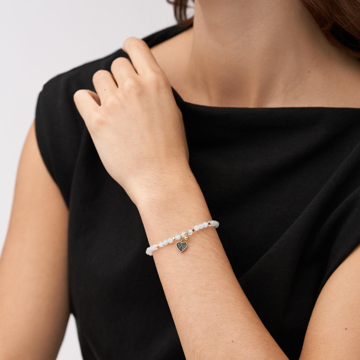 Rose quartz beaded bracelet on wrist with gold-tone heart charm and round medallion