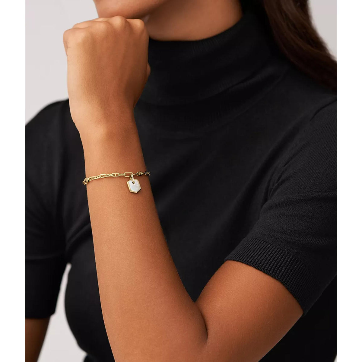 Gold-tone chain bracelet with square mother-of-pearl crest charm on wrist