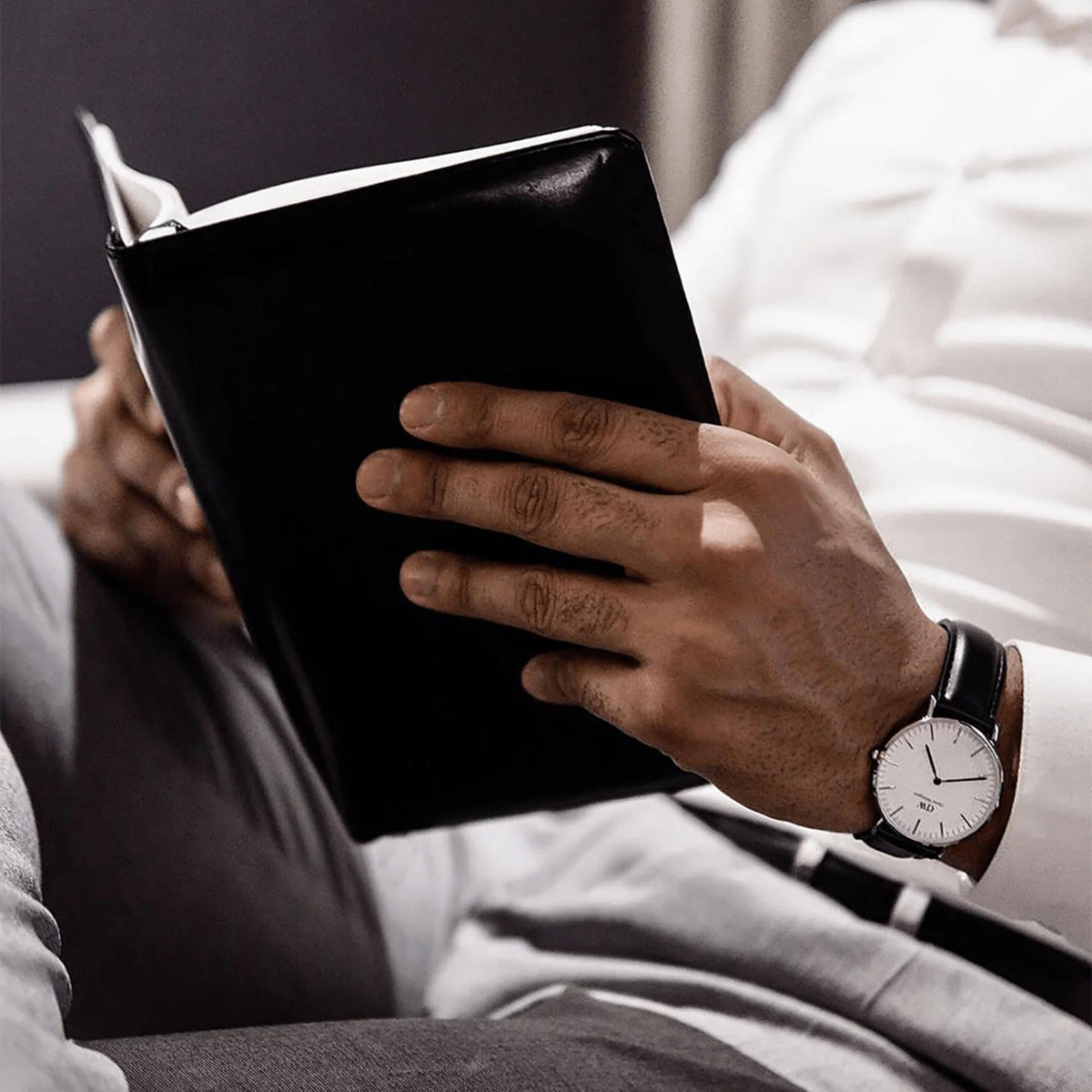Mens wrist watch with white dial and black leather strap worn on the arm