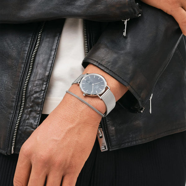 Daniel Wellington mens quartz watch on wrist with steel mesh bracelet and dark dial.