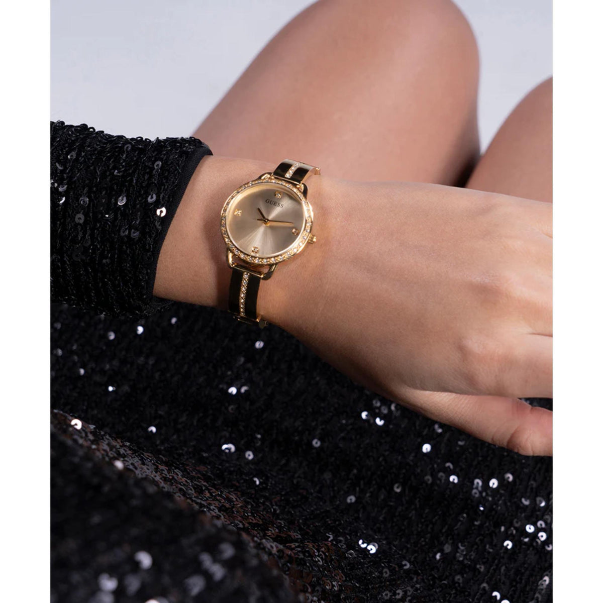Gold-tone analog watch on wrist with champagne dial, gem bezel, and metal bracelet.