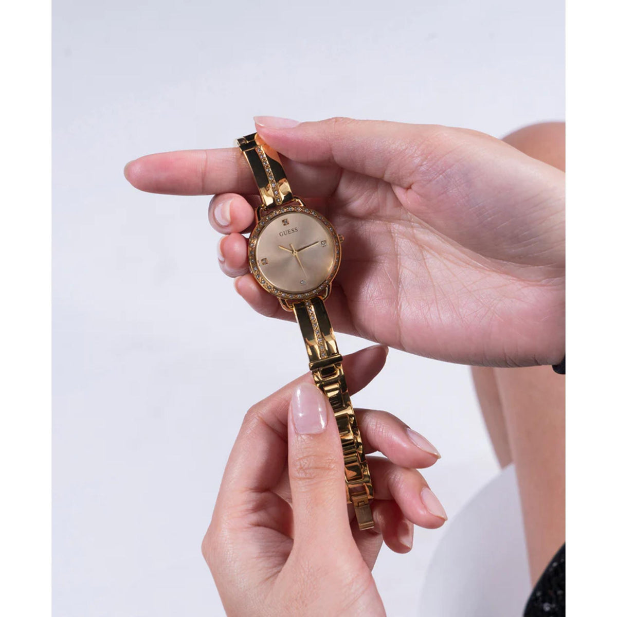 Gold-tone analog watch held in hands with champagne dial and linked metal bracelet.