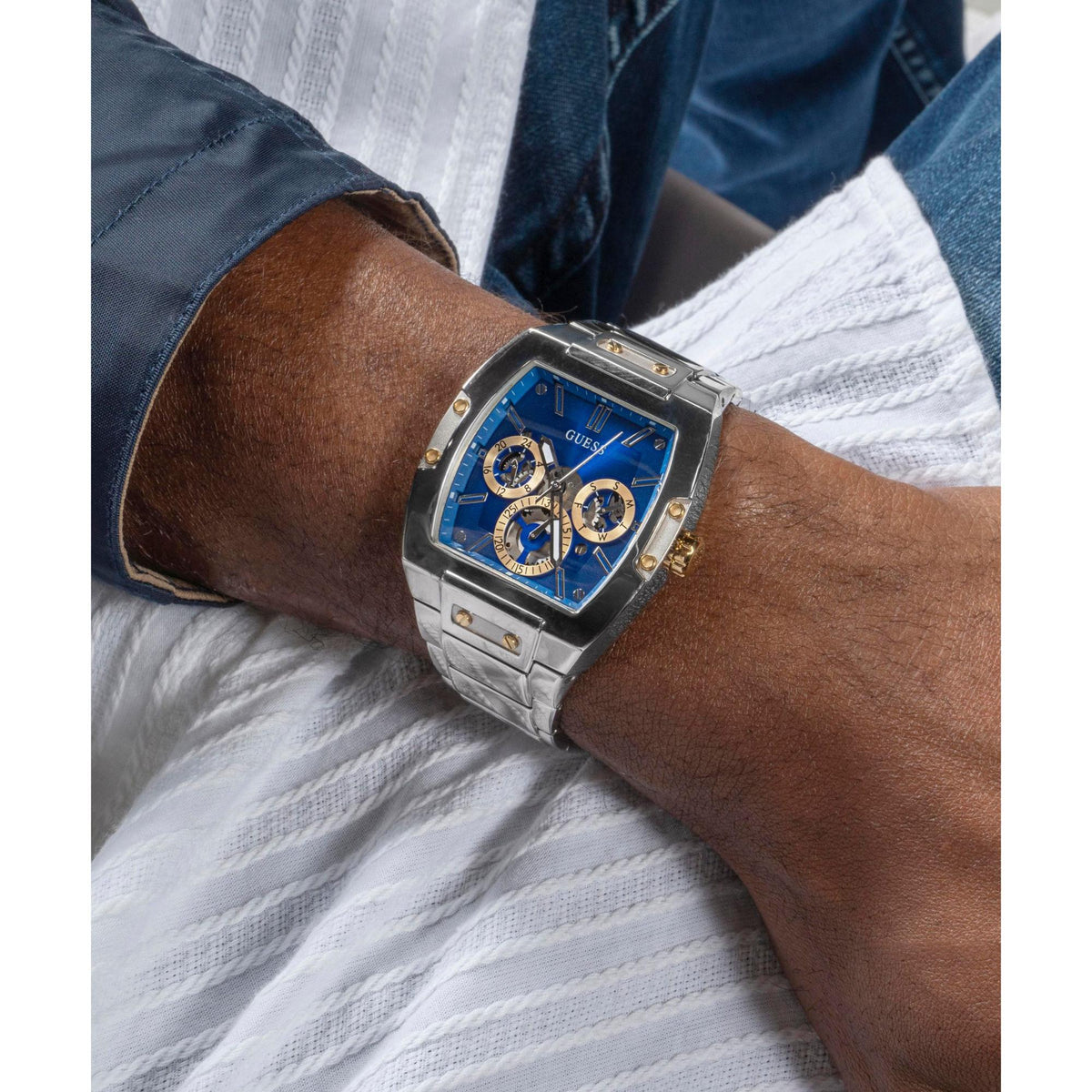 Blue dial multi-function watch on wrist with silver link bracelet and gold details.