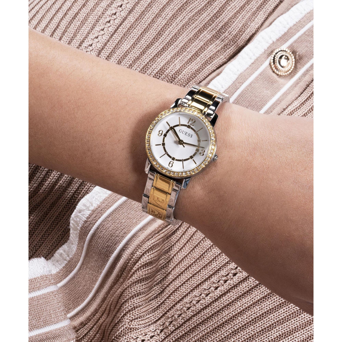 Two-tone analog watch on wrist with white dial, gold hands, and crystal-studded bezel