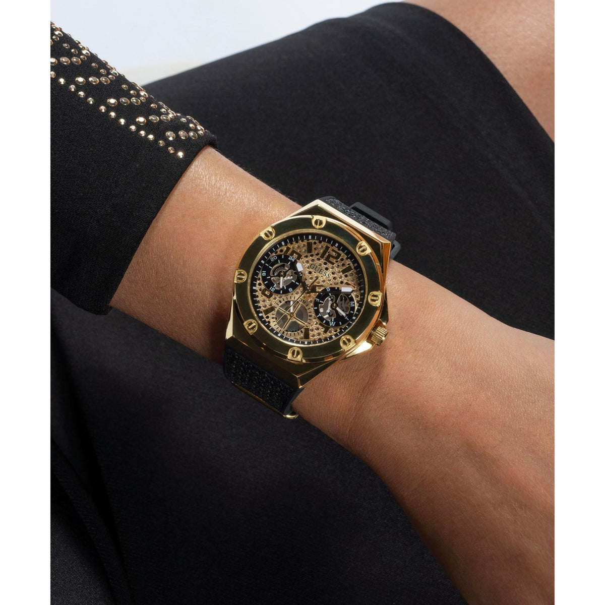 Gold-tone crystal dial watch on wrist with black silicone strap, three-quarter view