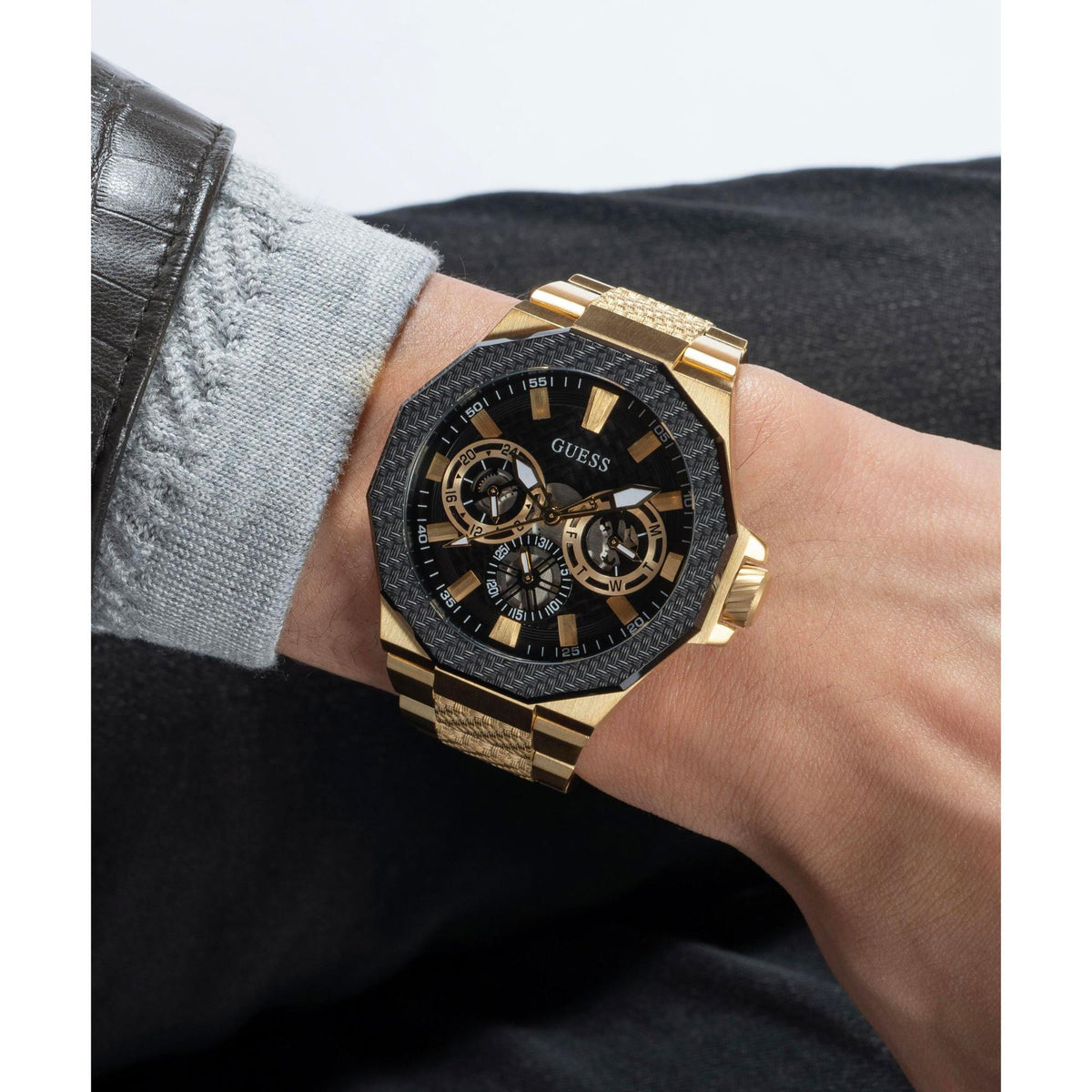 Two-tone men’s wristwatch on wrist; black dial with gold bezel and textured gold link band.