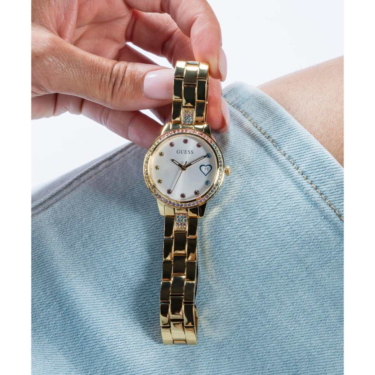 Gold tone ladies watch on wrist with white dial, crystal bezel, and date window on bracelet.