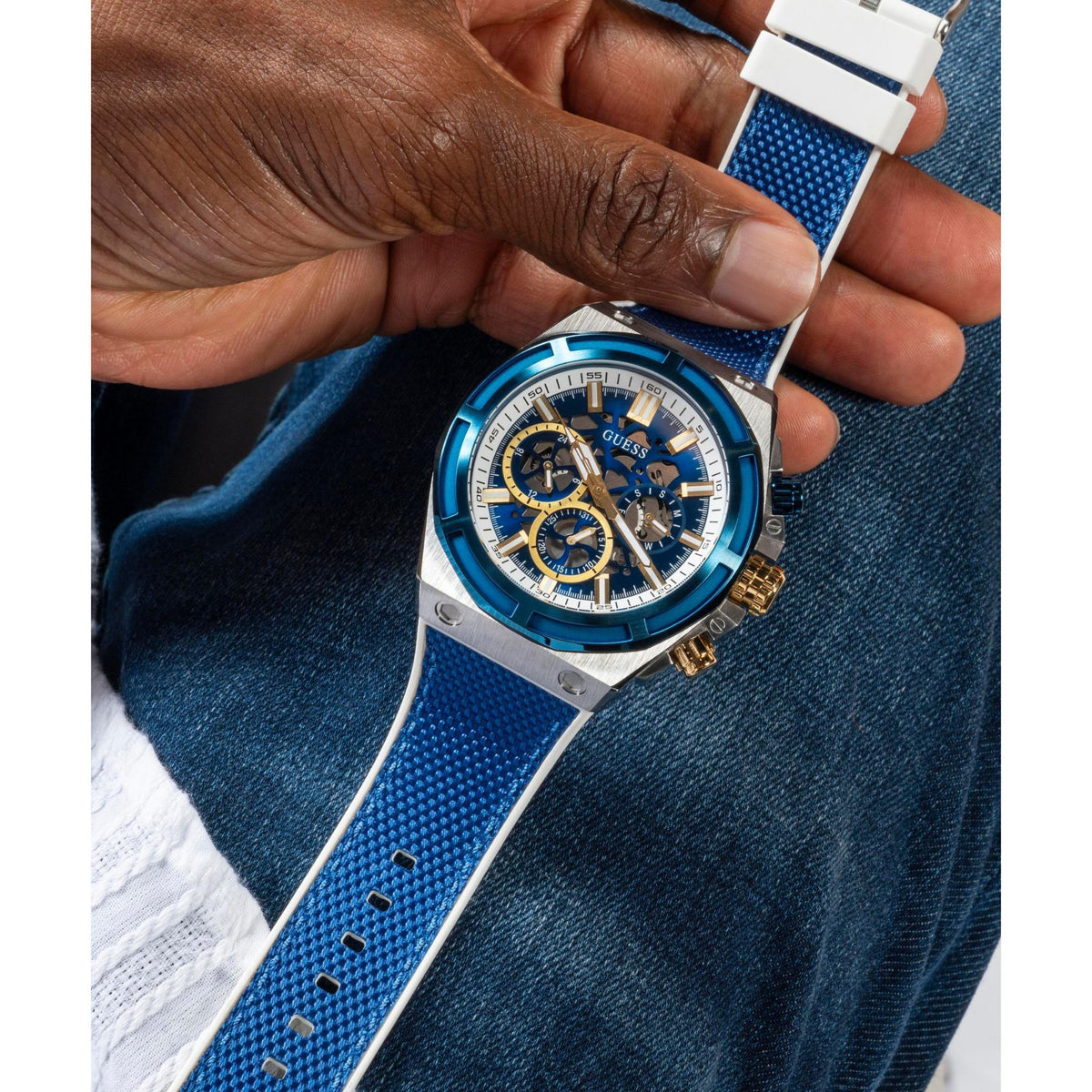 Men's chronograph watch on blue silicone strap held in hand, blue dial with subdials