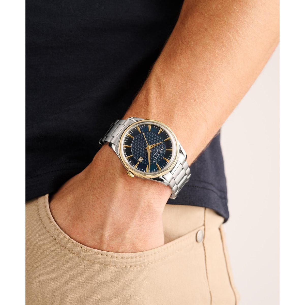 Men's stainless steel watch on wrist with blue dial, gold bezel, and link bracelet