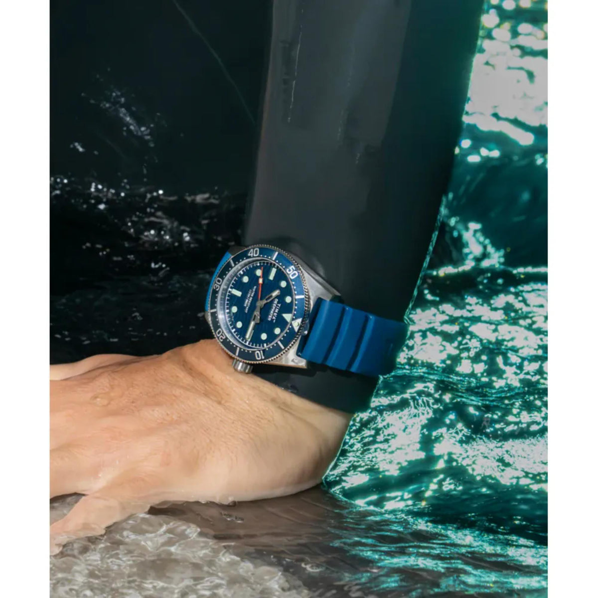 Men’s dive watch on wrist with dark blue bezel, dark dial, and blue rubber strap