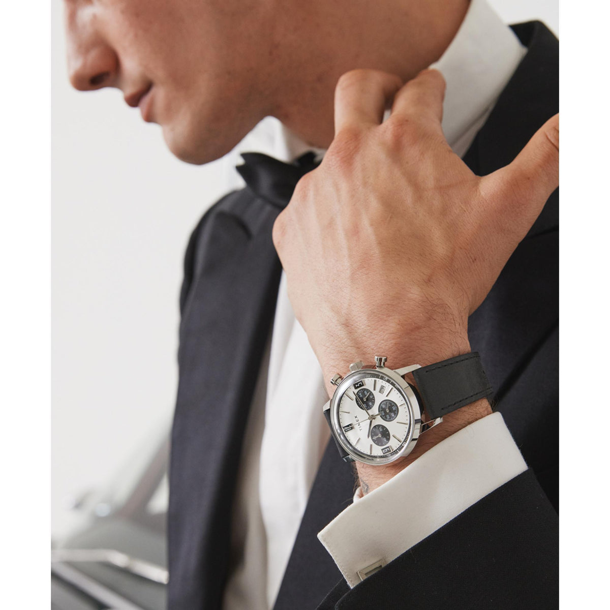 Men's silver chronograph watch on wrist with black leather strap and white dial