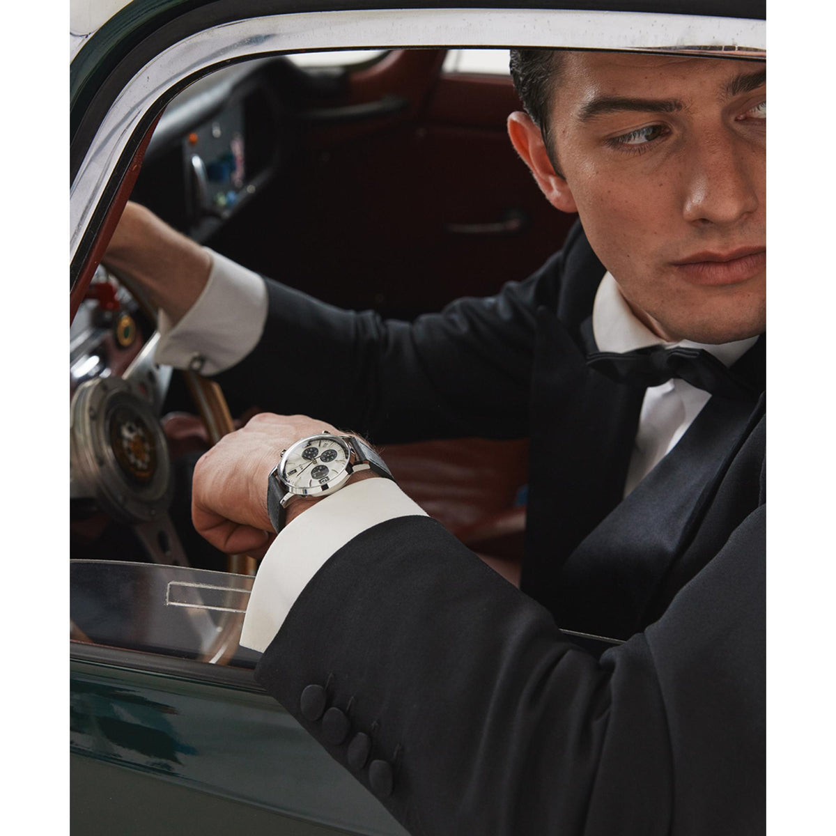 Men's chronograph watch on wrist in a suit, black leather strap and white dial visible