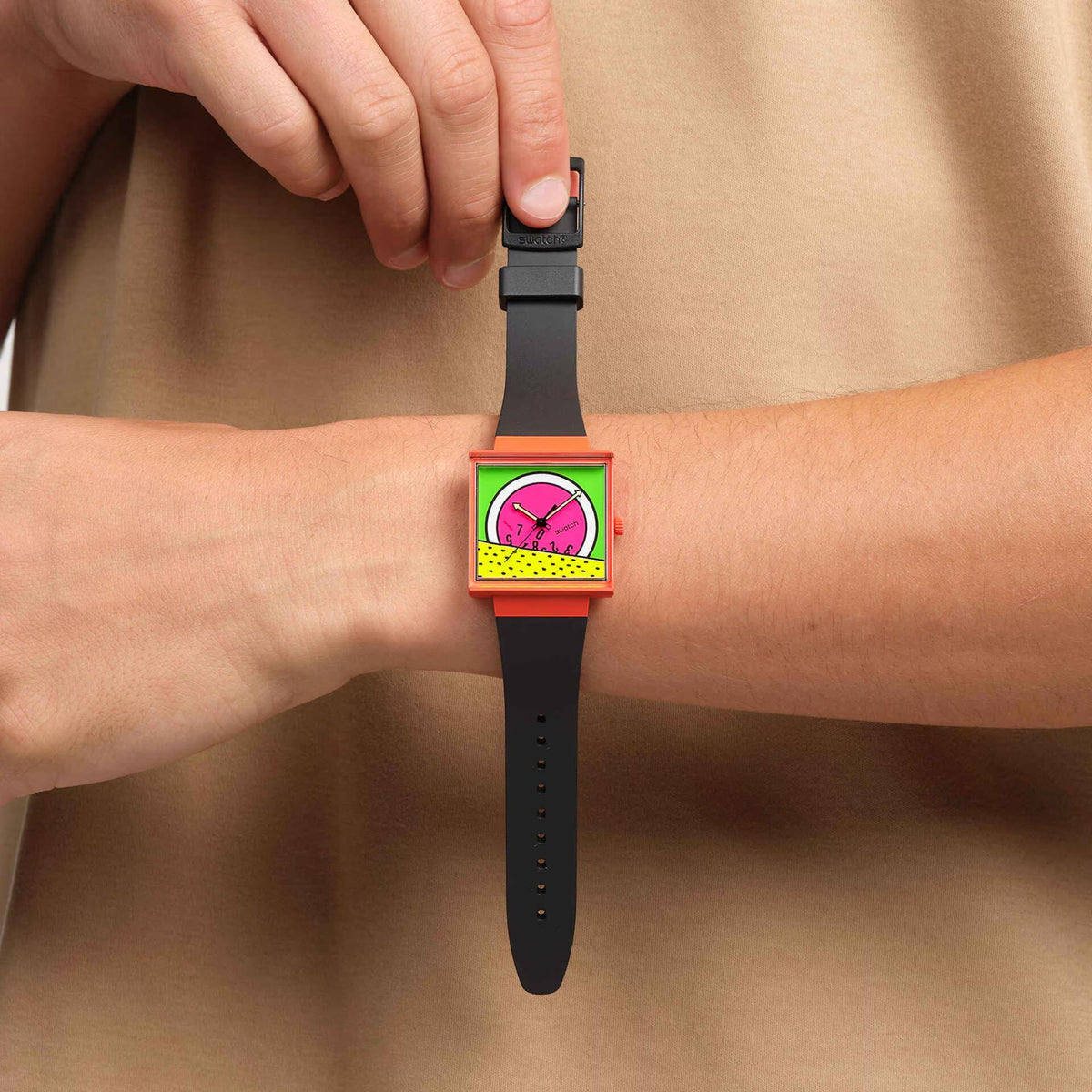 Women’s square Swatch watch on wrist with pink dial and black silicone strap