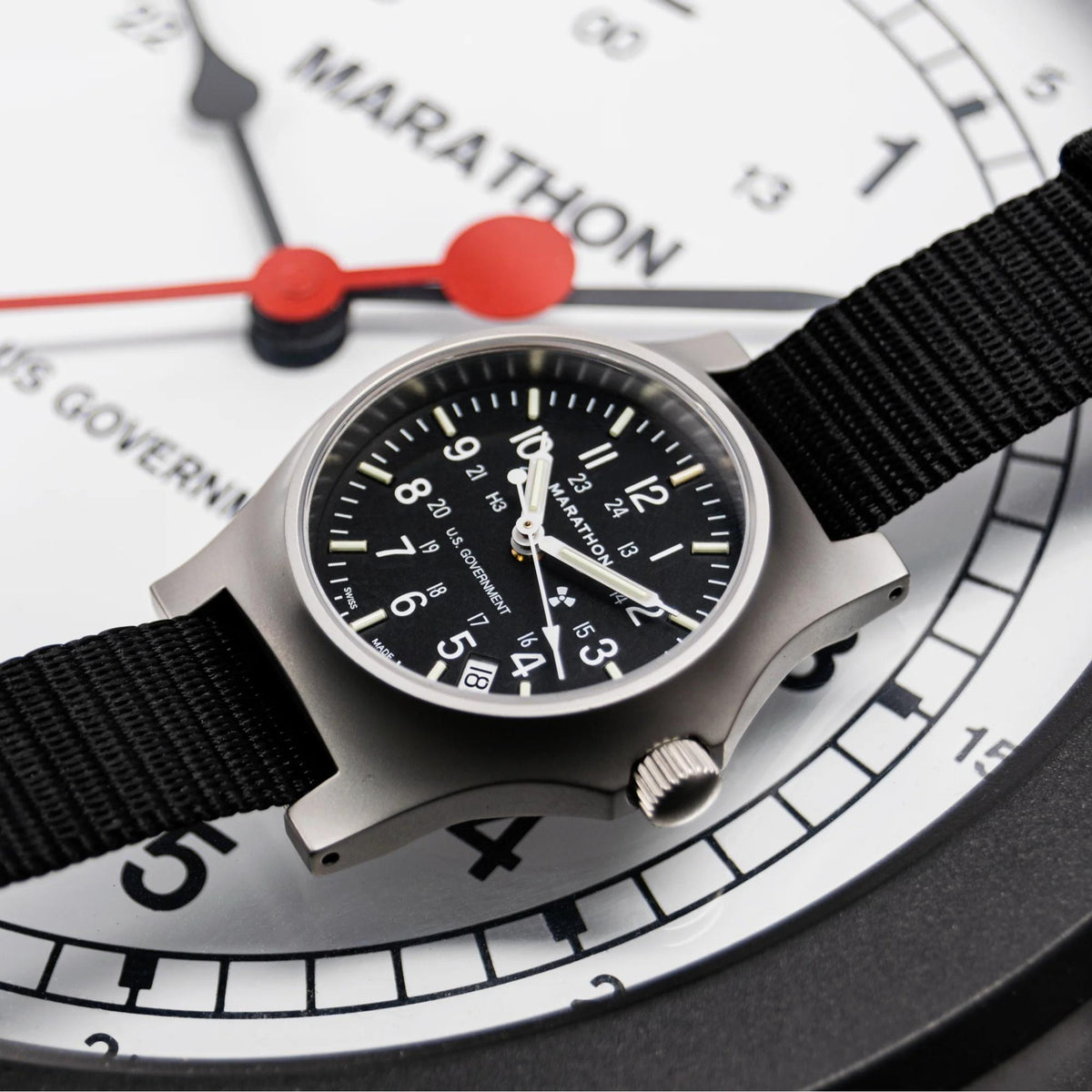 Quartz officer watch with black dial, silver case, and black fabric strap, angled view.