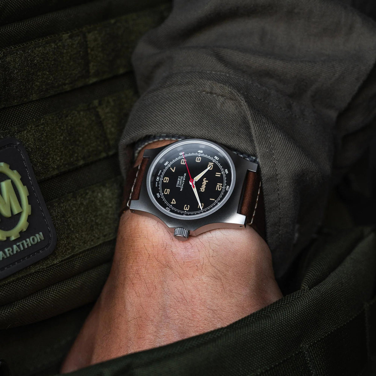 Men's quartz wristwatch on wrist; black dial, brown leather strap, stainless steel case.