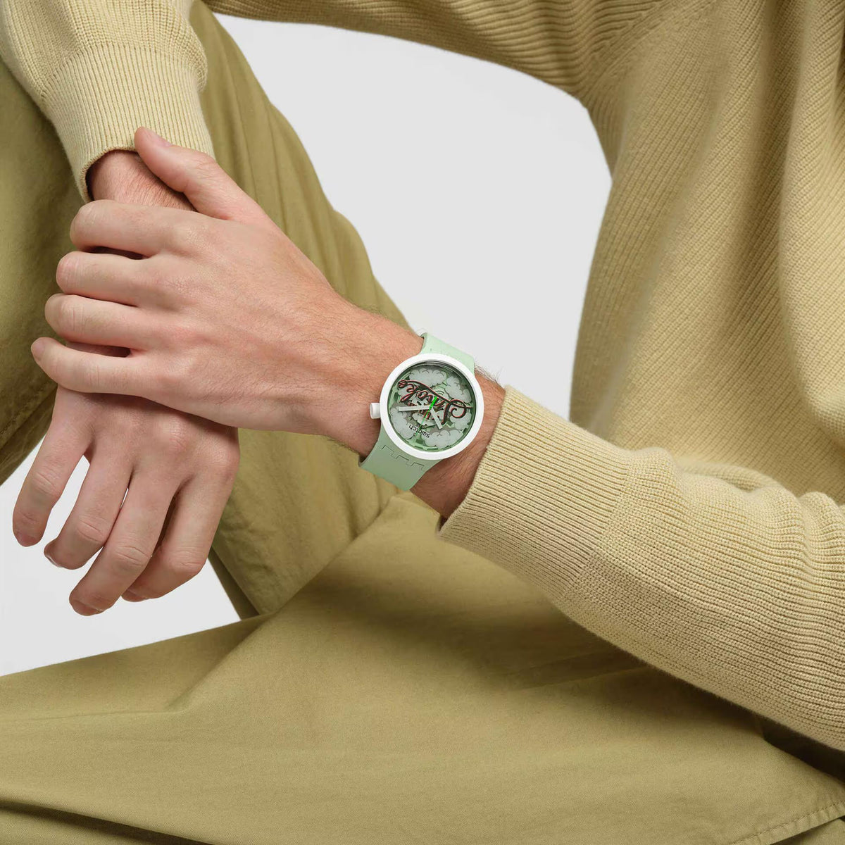 Mint green Swatch watch worn on wrist with round dial showing “Up in Smoke” and cloud motif