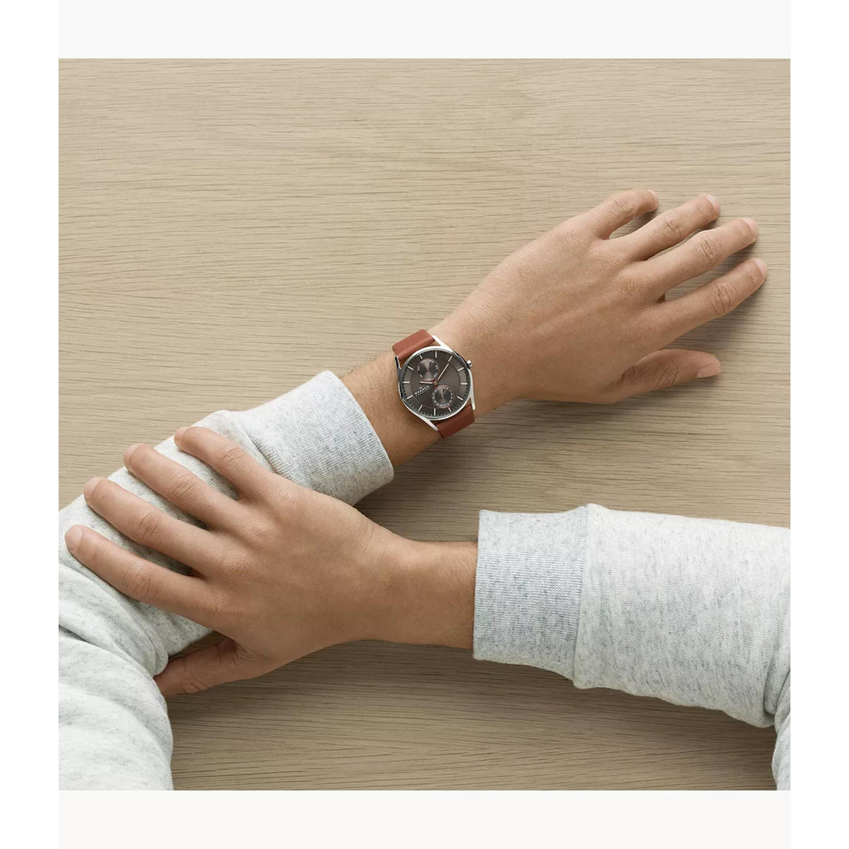 Men’s watch on wrist with brown leather strap and dark grey dial, hands resting