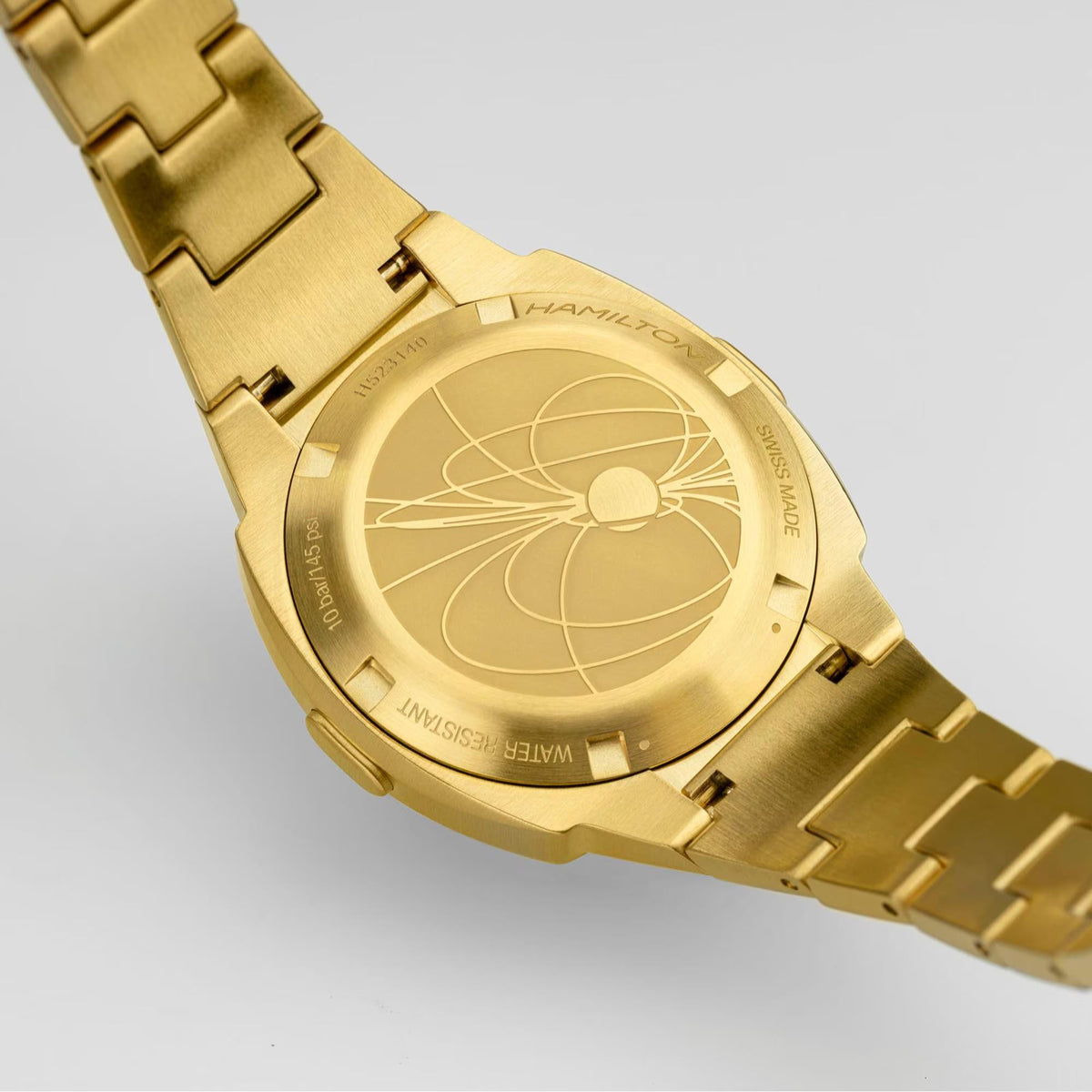 Gold watch caseback with engraved compass motif on metal link bracelet