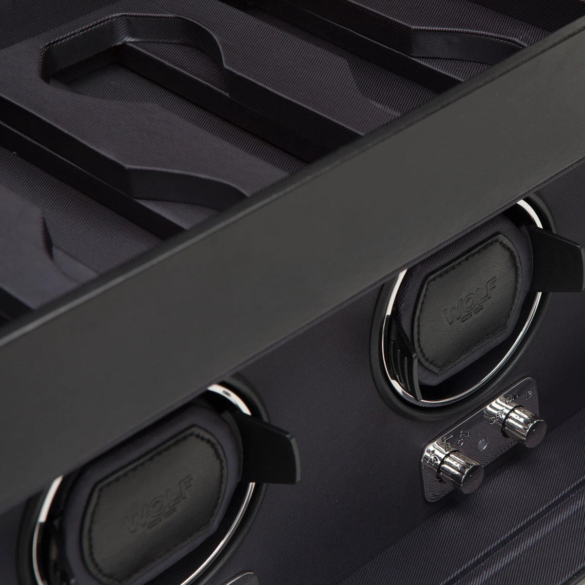 Close-up of three watch cradles and metal knobs inside a black winder.