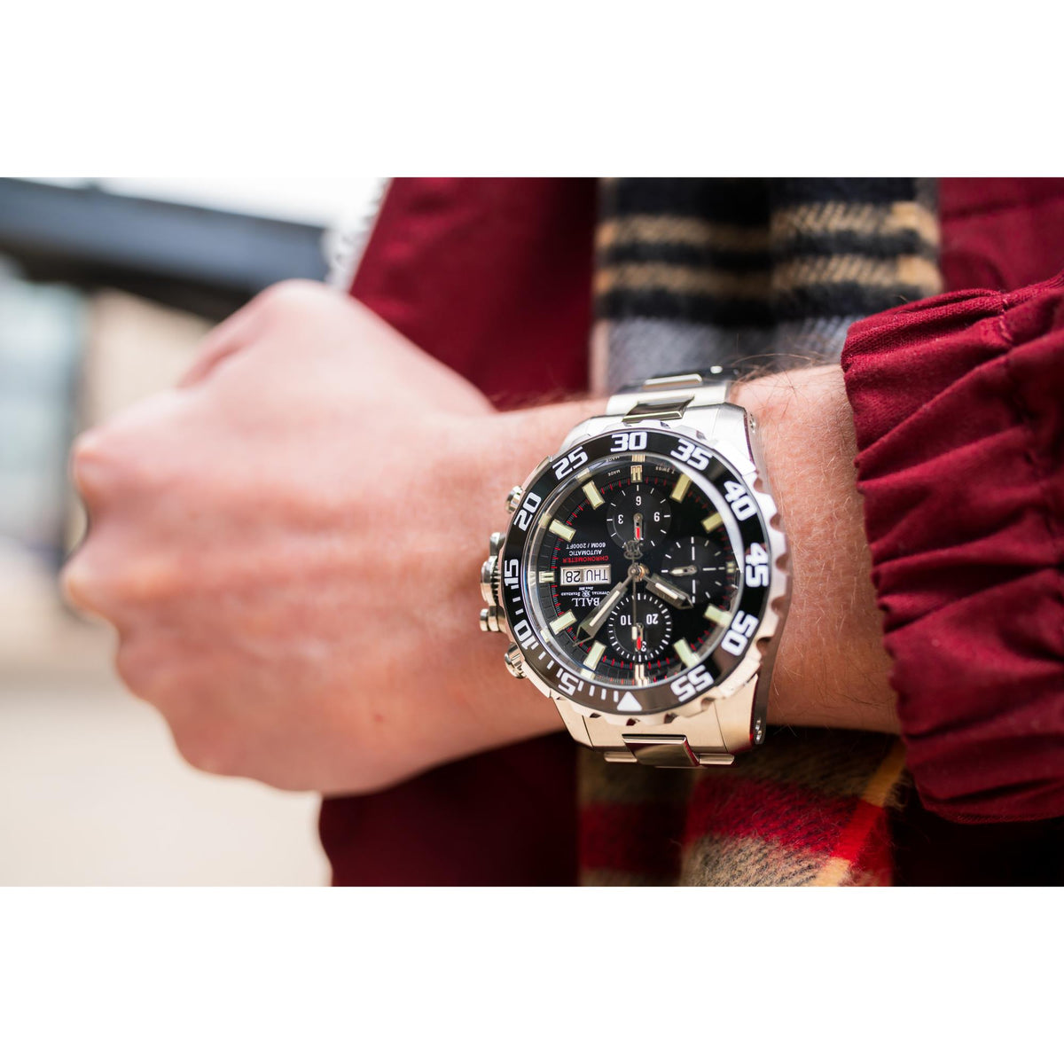 Men’s chronograph watch on wrist, black dial with subdials, steel bracelet and number-marked bezel.