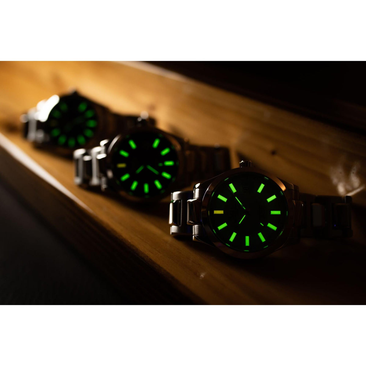 Three black sport watches with green luminous dials and metal bracelets