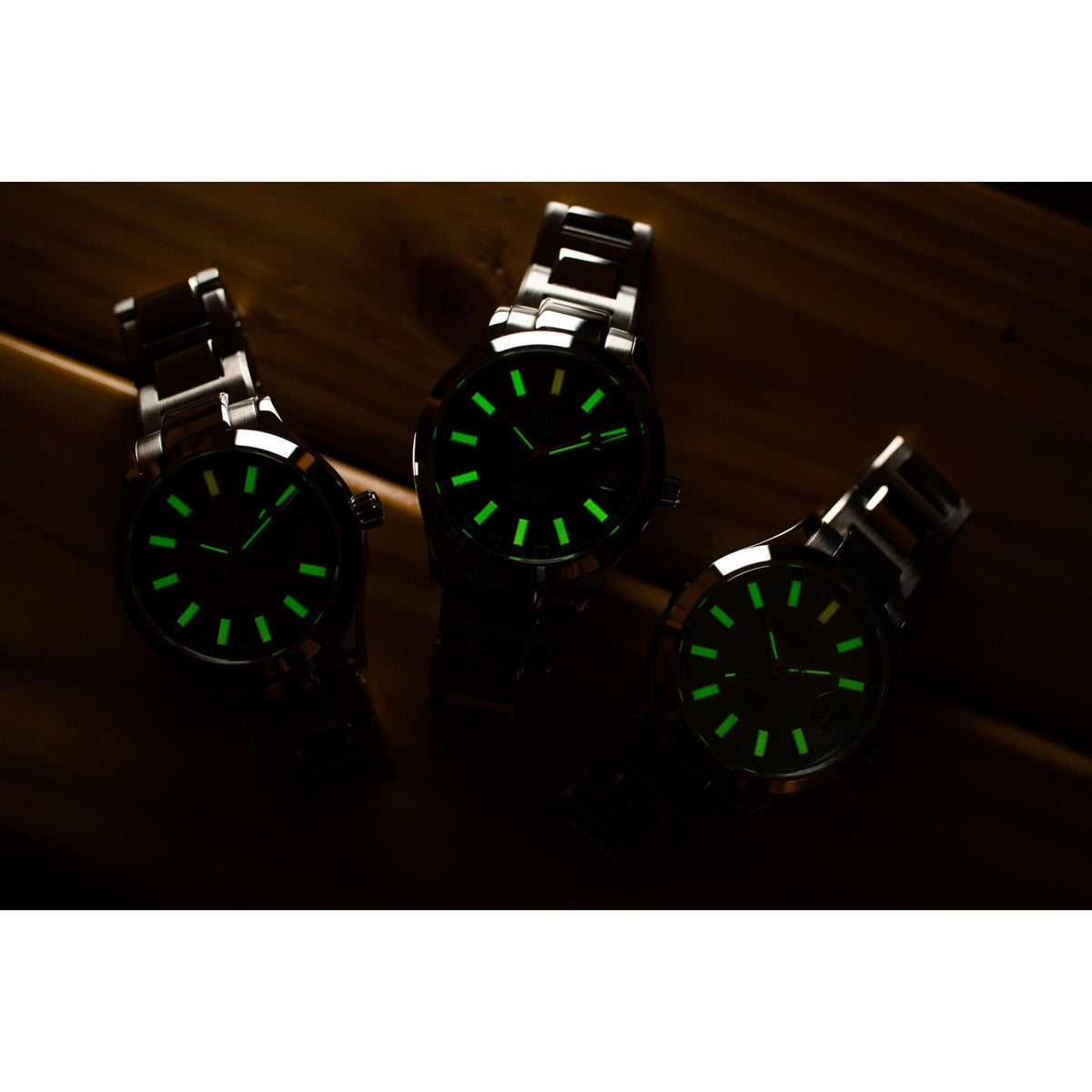 Three black sport watches with glowing green dial markers and metal bracelets