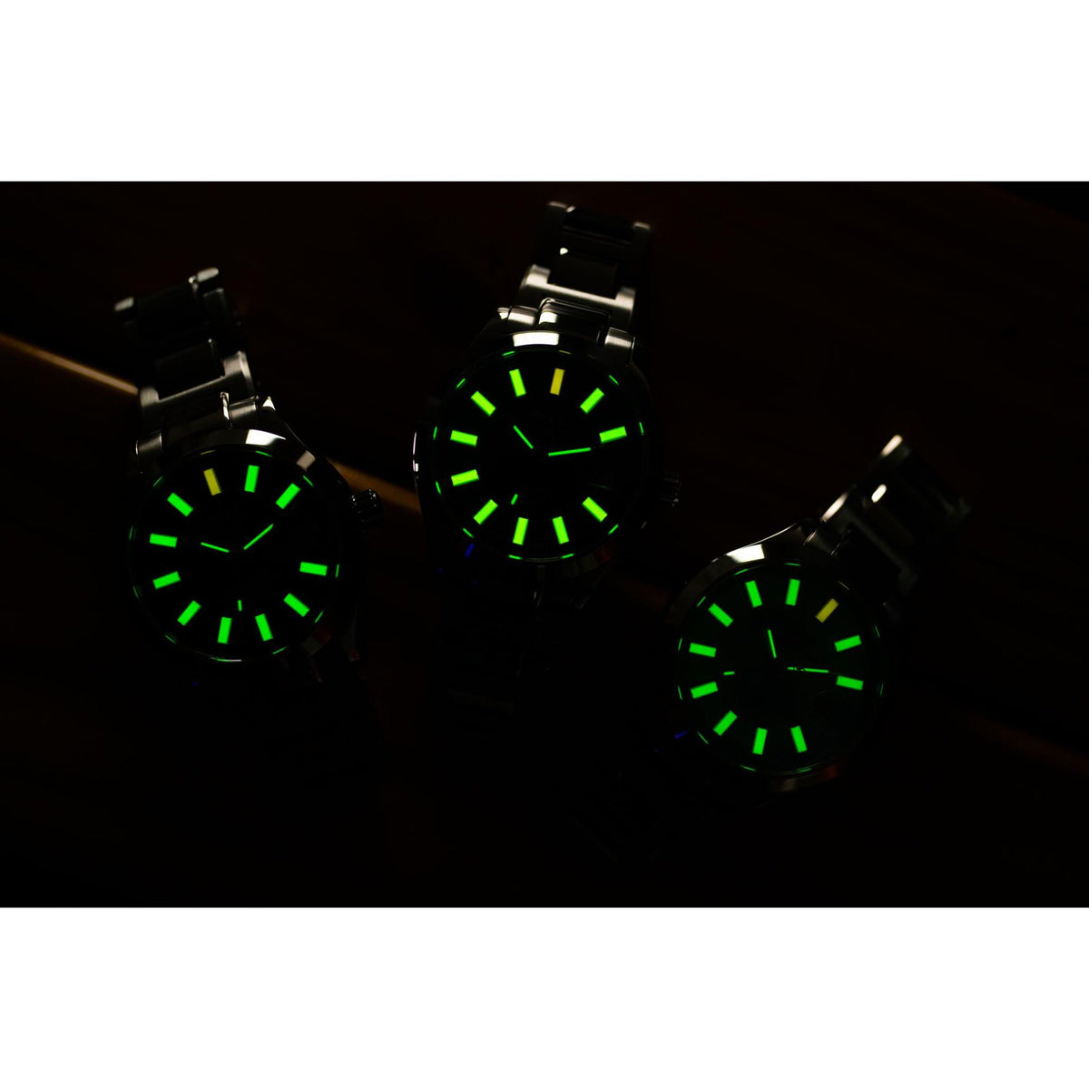 Three black sport watches with green luminous dial markers and metal bracelets