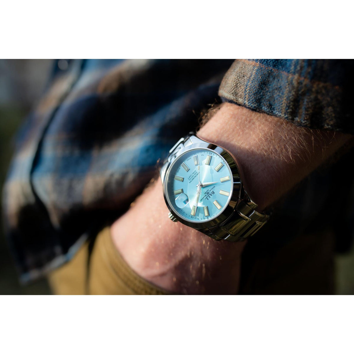 Men’s stainless steel watch with ice blue face and bracelet, worn on wrist in plaid