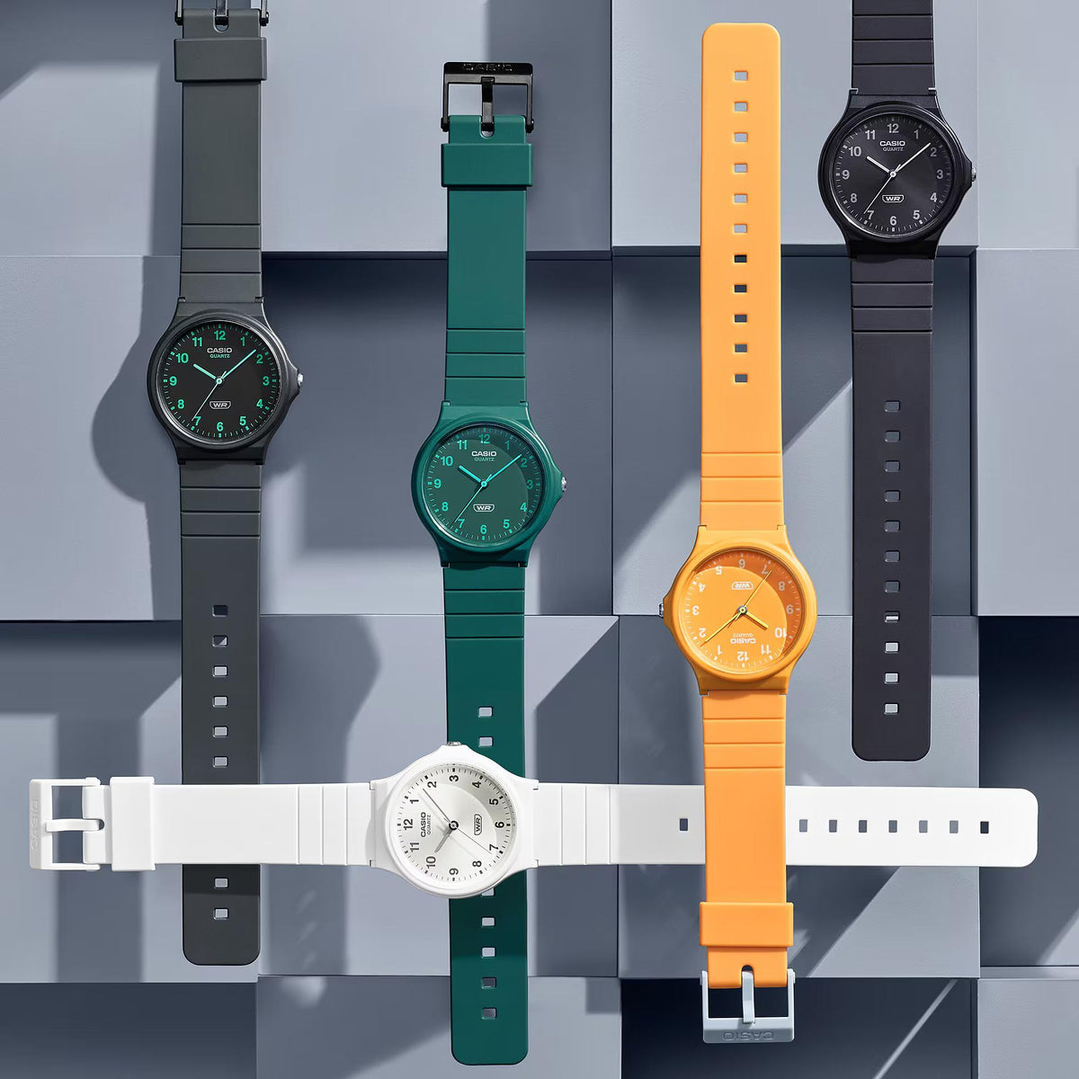 Flat lay display of the Casio Timeless Classic MQ-24B-3BEF green watch alongside other colorways on a segmented block backdrop