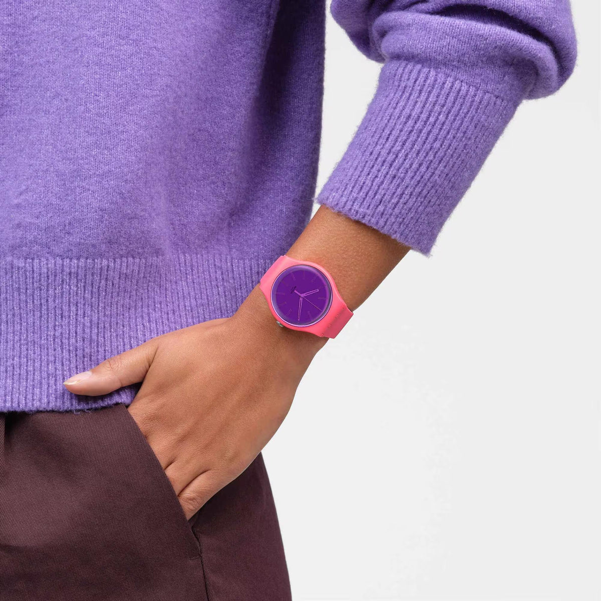Swatch pink silicone watch on wrist with purple dial and hands under a sleeve
