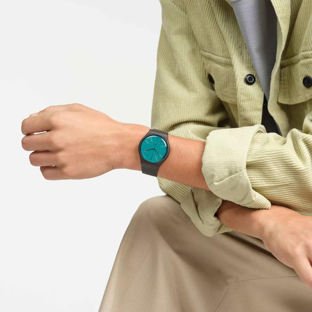 Teal-dial analog wristwatch on dark brown strap worn on wrist with knit sleeve.