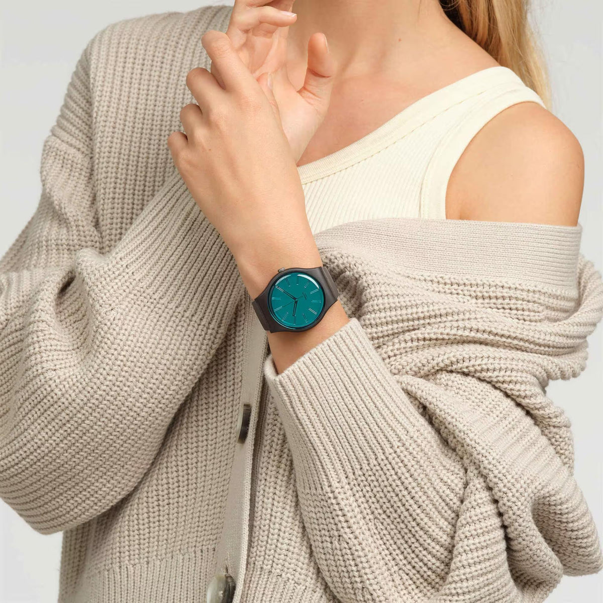 Teal-dial analog wristwatch on dark brown strap worn under cream knit sweater cuff.